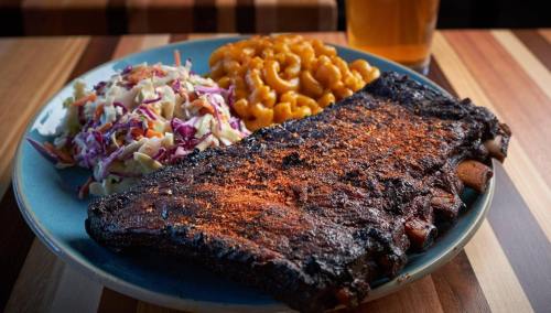 A plate of BBQ ribs with a side of macaroni and cheese and coleslaw, accompanied by a glass of beer.