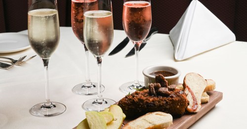 A wooden platter with fried chicken, bread, and apples, accompanied by sparkling drinks in fluted glasses.