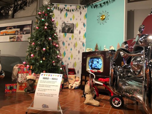 A vintage holiday display featuring a Christmas tree, retro TV, gifts, and classic cars from the 1950s.