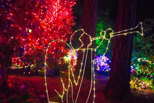 A glowing angel figure playing a trumpet, surrounded by colorful holiday lights in a forest setting.