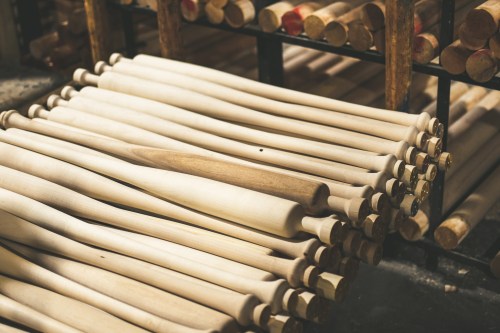 A stack of unfinished wooden baseball bats arranged neatly on a shelf in a workshop.