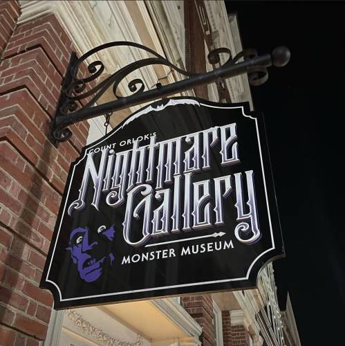 Sign for "Nightmare Gallery Monster Museum" featuring a stylized face, hanging from a brick building.