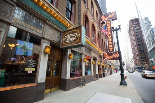 Exterior of a restaurant on a city street, featuring a sign that reads "Adams Street" and "The Breakfast Restaurant."