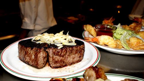 A perfectly cooked steak topped with sliced onions, served alongside shrimp and dipping sauce on a plate.