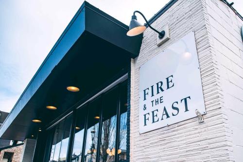 Exterior of a restaurant with a sign that reads "FIRE & THE FEAST," featuring large windows and modern lighting.