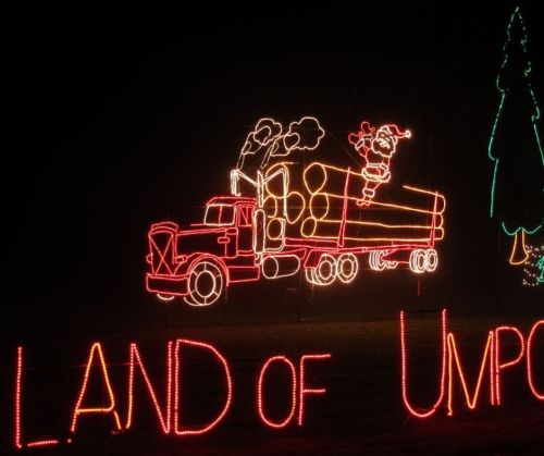 A brightly lit truck carrying logs with Santa on top, surrounded by festive holiday lights. Text reads "LAND OF UN."
