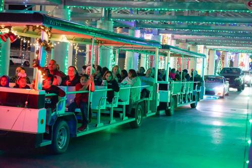 A festive train filled with people rides through a brightly lit area decorated with colorful lights.
