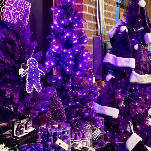Purple-themed holiday display featuring decorated trees, hats, and ornaments, all illuminated with purple lights.