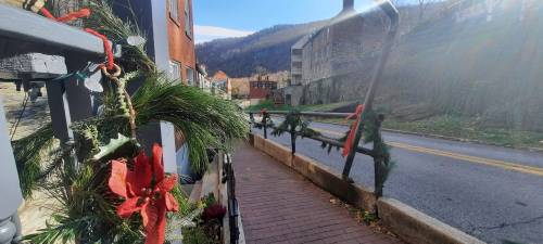 A decorated walkway with holiday greenery, leading to a street and mountains in the background under a clear sky.