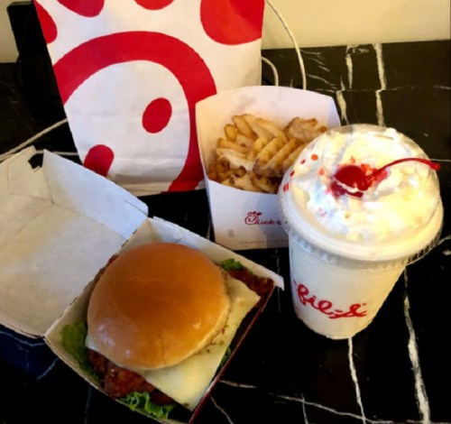 A Chick-fil-A meal featuring a sandwich, waffle fries, and a milkshake topped with whipped cream and a cherry.