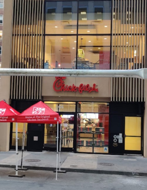 Exterior of a Chick-fil-A restaurant with red canopies at the entrance and large windows showcasing the interior.