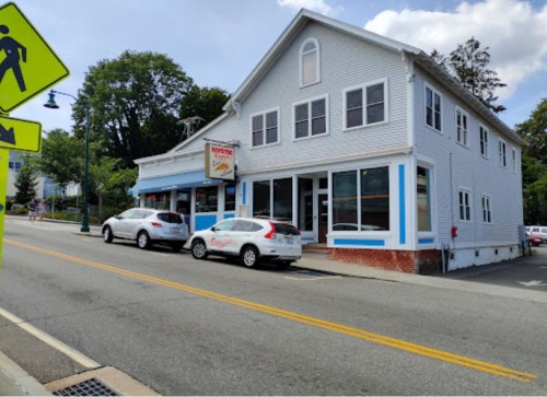 A white two-story building with blue trim, featuring a storefront and parked cars on a sunny street.