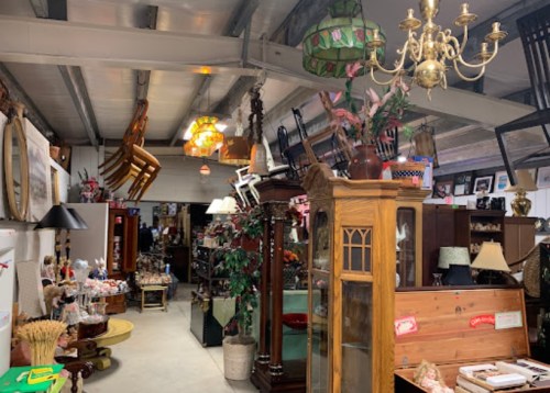 A spacious antique shop filled with various vintage furniture, lamps, and decor items hanging from the ceiling.