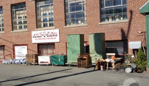 A brick building with large windows displays various vintage furniture and items outside, including cabinets and chairs.