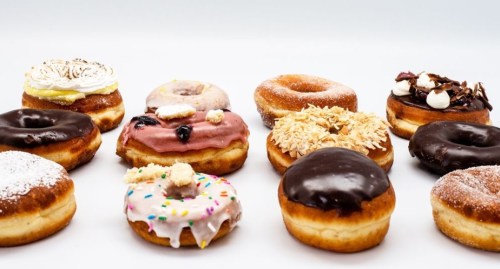 A variety of colorful donuts with different toppings arranged on a white background.