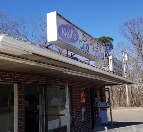 Sign for Neil's Donut Bakery & Sundries on a brick building, with a clear blue sky in the background.