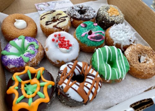 A box of assorted colorful donuts with various toppings and designs, including sprinkles and icing.