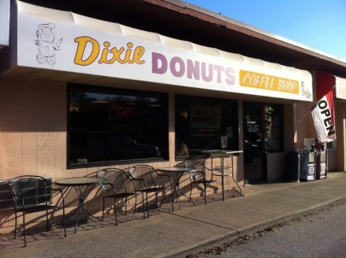 Exterior of Dixie Donuts coffee shop with a sign reading "Open" and outdoor seating.