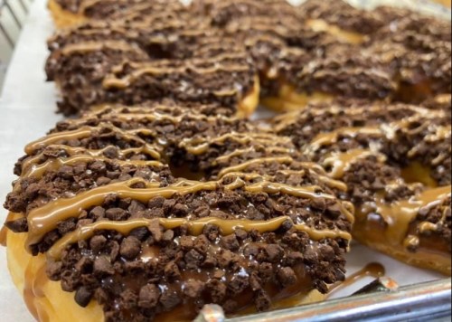 Close-up of chocolate-covered donuts topped with crushed cookies and drizzled with caramel sauce.