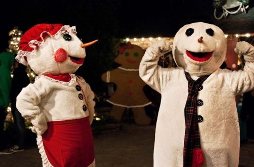 Two cheerful snowman mascots in festive attire, posing playfully in a decorated holiday setting.