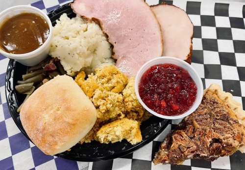 A plate of food featuring turkey, mashed potatoes, green beans, cornbread, cranberry sauce, and pecan pie.
