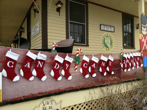 A festive display of red and white stockings hanging on a railing, with candy canes and holly decorations.