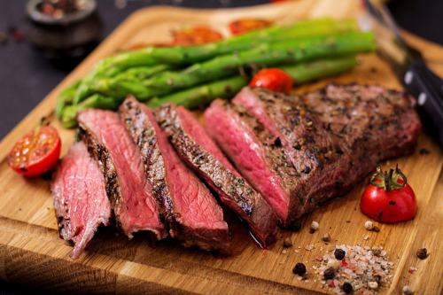 Sliced grilled steak on a wooden board, accompanied by asparagus and cherry tomatoes.