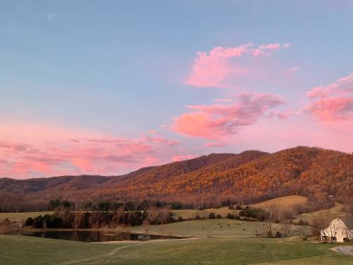 A serene landscape featuring rolling hills, a calm pond, and a colorful sunset with pink and orange clouds.