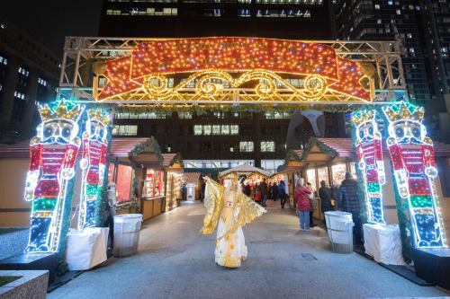 A festive market entrance adorned with colorful lights and decorations, with a person in a bright costume walking through.