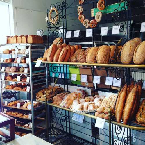 A bakery display featuring various breads and pastries on shelves, including loaves, rolls, and donuts.