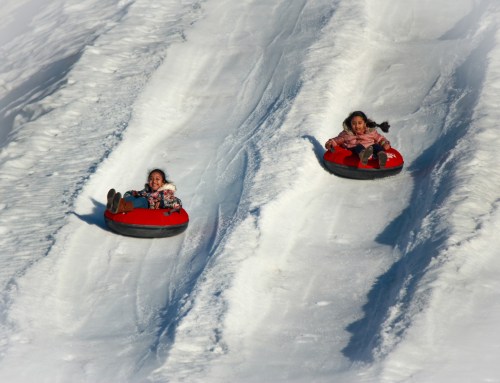Two children slide down a snowy hill on red snow tubes, enjoying a fun winter day.