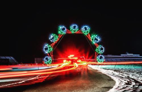Colorful light arch with festive decorations, glowing against a dark night sky, with car lights creating streaks.