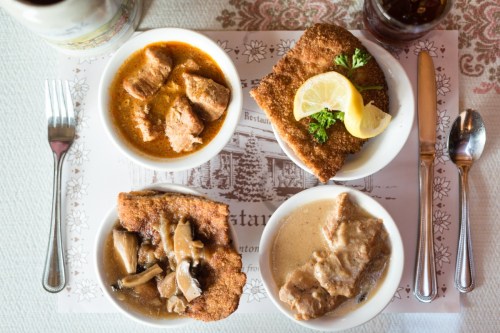 A table setting with four dishes: breaded meat, stew, and two creamy sauces, garnished with lemon and herbs.