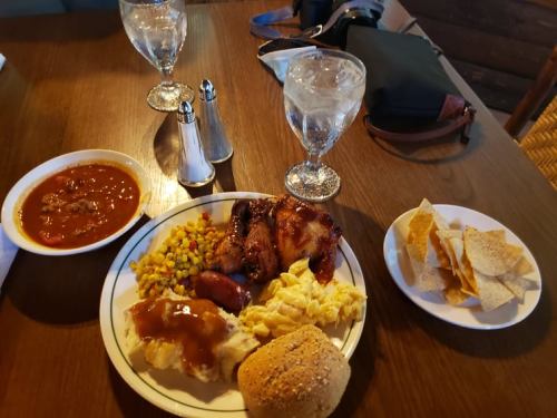 A plate of food featuring chicken, corn, mashed potatoes, a roll, chili, and tortilla chips, with two glasses of water.