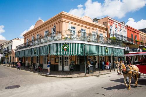 A historic building with green and white striped awnings, people outside, and a horse-drawn carriage on the street.