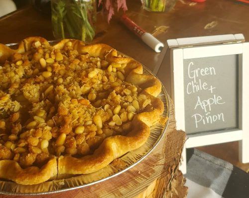A delicious green chile and apple pinon pie on a wooden table, with a small chalkboard sign displaying its name.