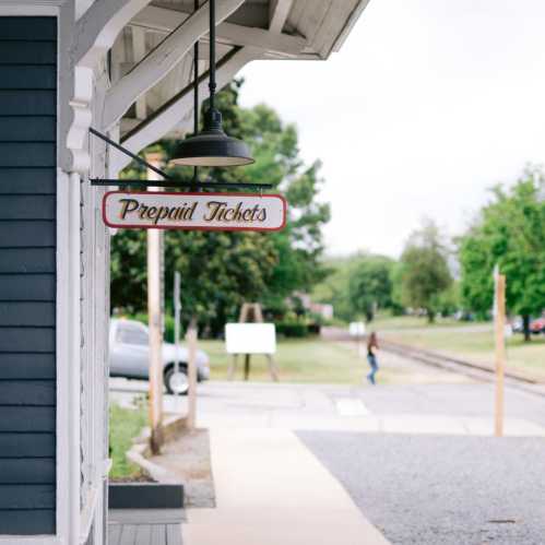 A sign reading "Prepaid Tickets" hangs from a building, with greenery and a pathway visible in the background.