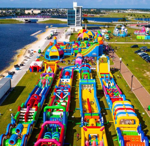 Aerial view of a colorful inflatable water park with slides and play areas by a lake on a sunny day.
