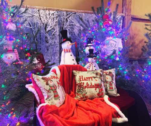 Cozy holiday scene with a decorated sofa, festive pillows, snowmen, and colorful lights on trees.