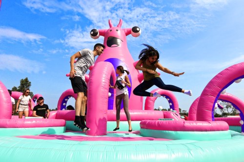 A colorful inflatable bounce house with people jumping and playing under a blue sky.