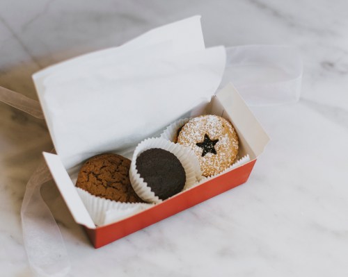 A red box containing three assorted cookies, including a star-shaped cookie, on a marble surface.