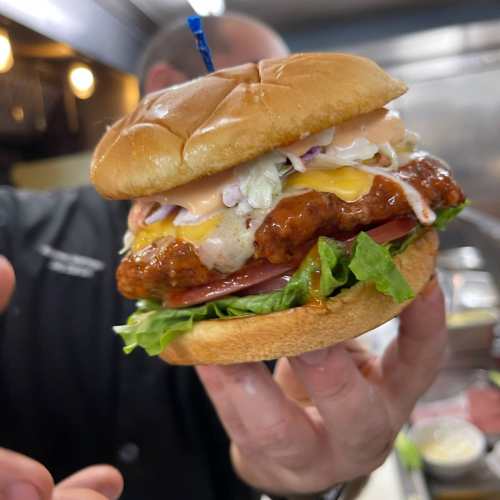 A person holds a delicious sandwich with crispy chicken, lettuce, cheese, and sauce, served on a toasted bun.