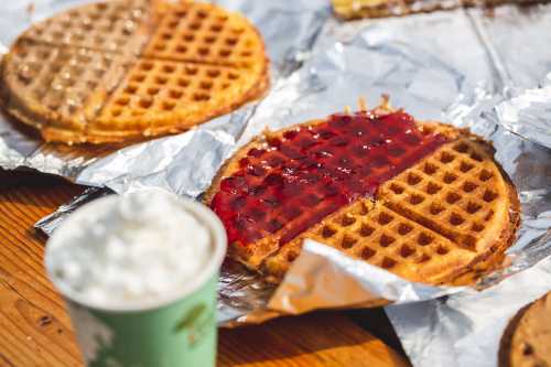 Waffles topped with jelly, placed on foil, with a cup of whipped cream in the foreground.