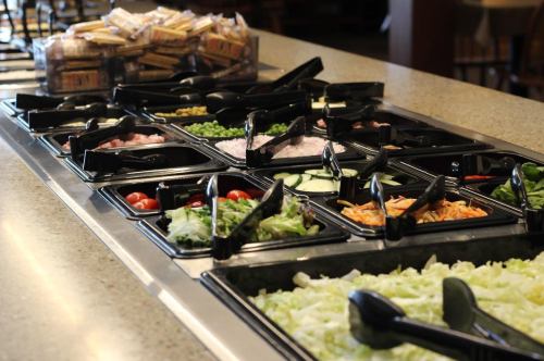 A salad bar with various toppings in black containers, including greens, tomatoes, and peas, on a countertop.