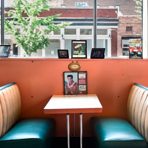 A cozy diner with teal booths, a small table, and vintage photos on the wall, including an Elvis memorabilia piece.