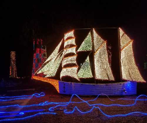 A brightly lit sailboat made of colorful lights, surrounded by glowing blue waves, set against a dark night sky.