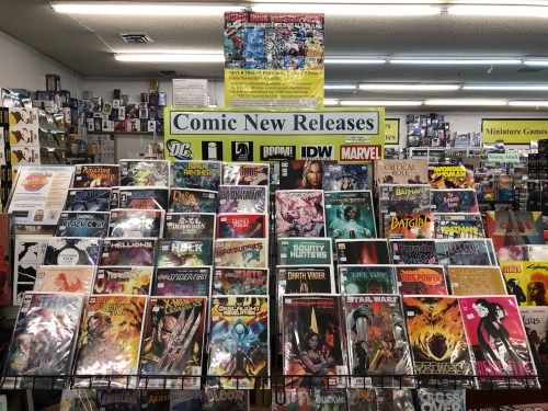 A display of new comic book releases featuring various titles from DC, Marvel, and other publishers in a store.