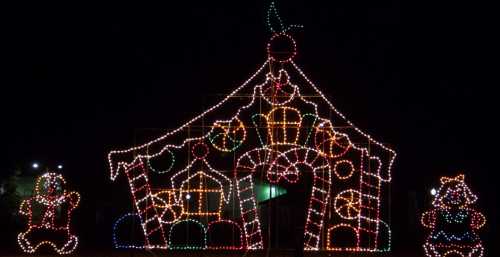 Colorful holiday lights form a gingerbread house with candy decorations and cheerful figures on either side.