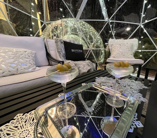 A cozy igloo-like setting with two martini glasses on a tray, surrounded by plush seating and twinkling lights.