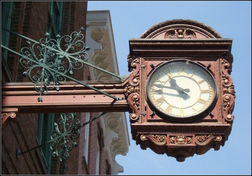 Vintage clock mounted on a decorative bracket, showing the time against a clear blue sky.
